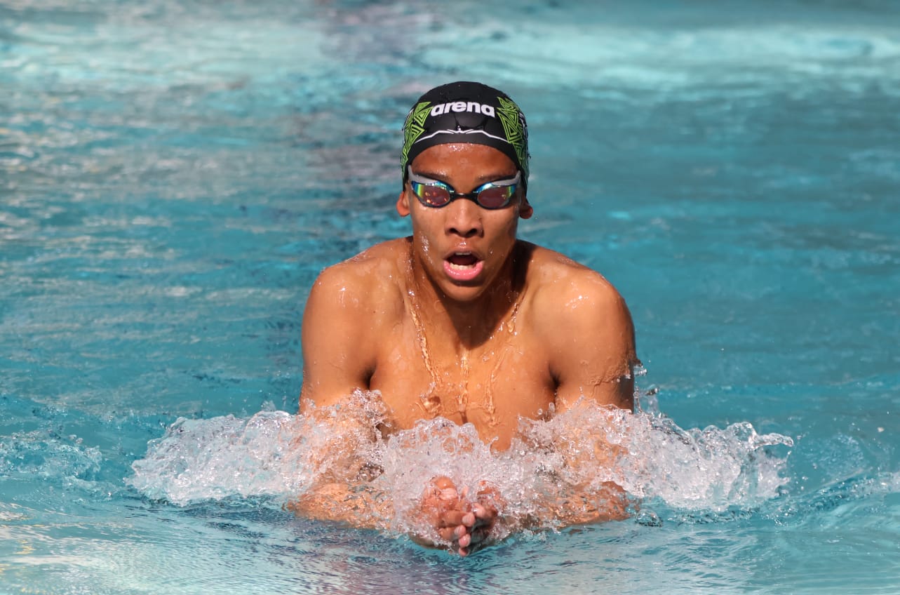 Person swimming in a pool wearing an Arena swim cap and goggles.