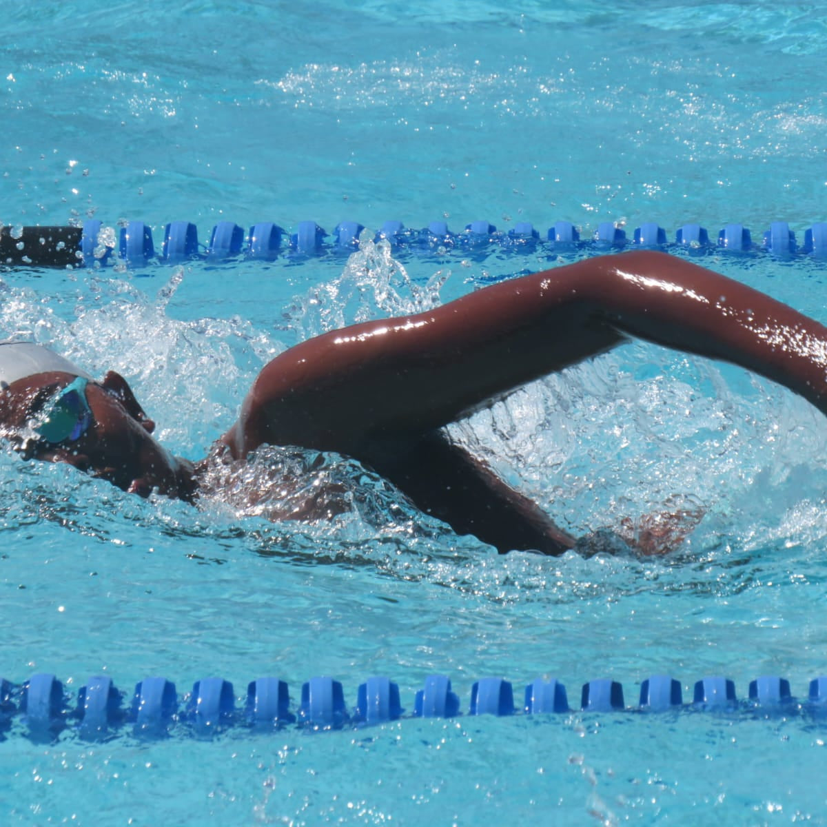 Person swimming in a pool with blue water and lane dividers.